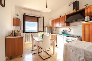 Une cuisine avec des meubles en bois, une cuisinière à gaz, une table à manger blanche avec des chaises, et une vue par la fenêtre.