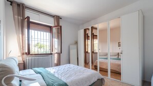 Un dormitorio con cama, radiador, ventana con cortinas y armario con puerta corredera.
