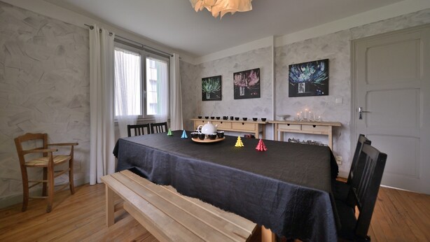 A room with a dining table, chairs, a bench, a window with curtains, and wall-mounted artwork. - Luchon : maison flor (Bagnères-de-Luchon)