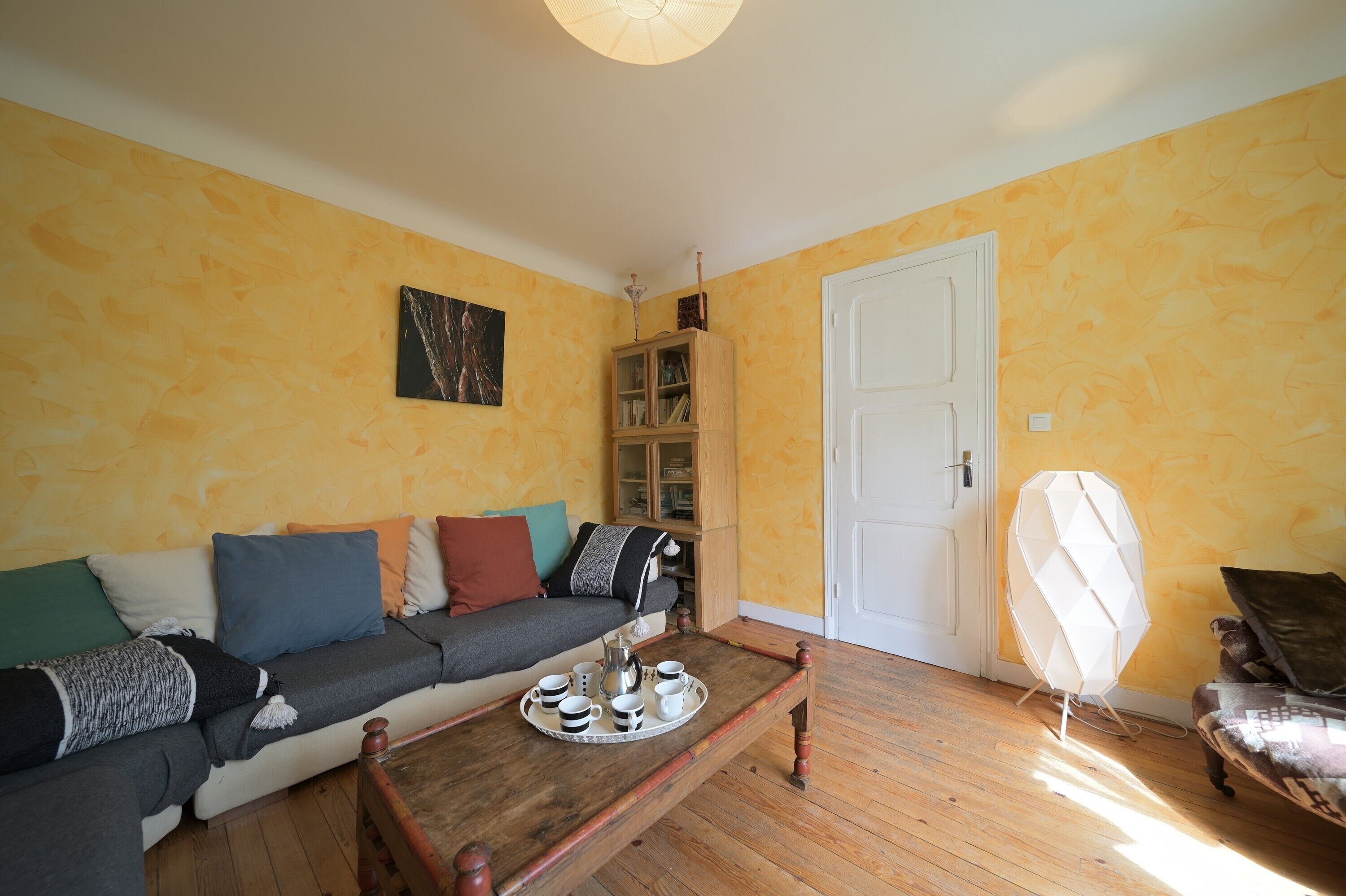 Ein Wohnzimmer mit einer Couch, einem Couchtisch mit einer Kaffeetasse und einem Teekessel, einem Schrank und einer Tür.