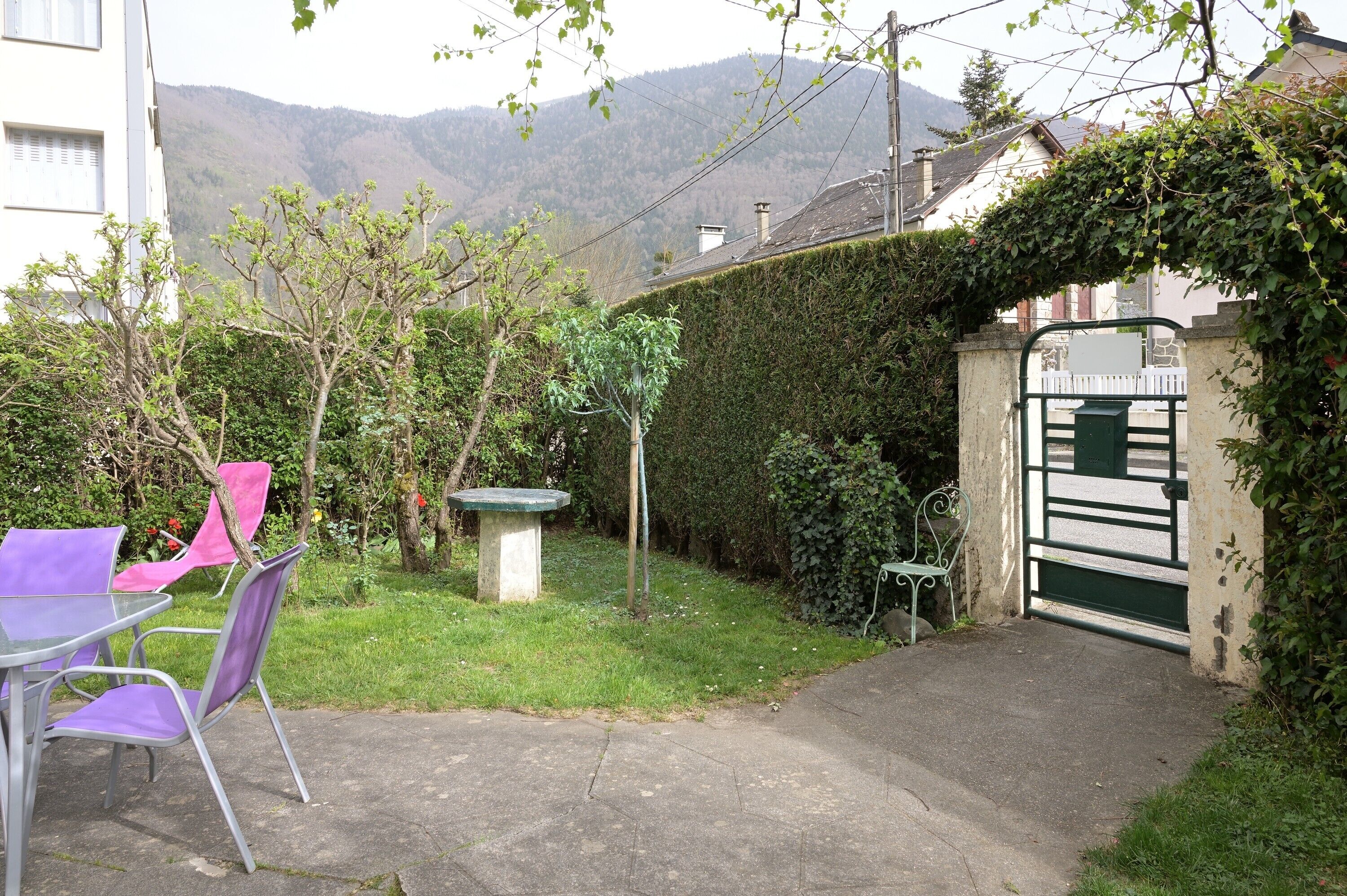 Un jardin avec une table et des chaises, un banc, une porte et une haie.