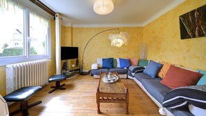 A living room with a sofa, a coffee table, a bench, a floor lamp, and a radiator. - Luchon : maison flor (Bagnères-de-Luchon)