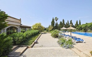 A pool area with lounge chairs, a building with a stone facade, and a clear sky.