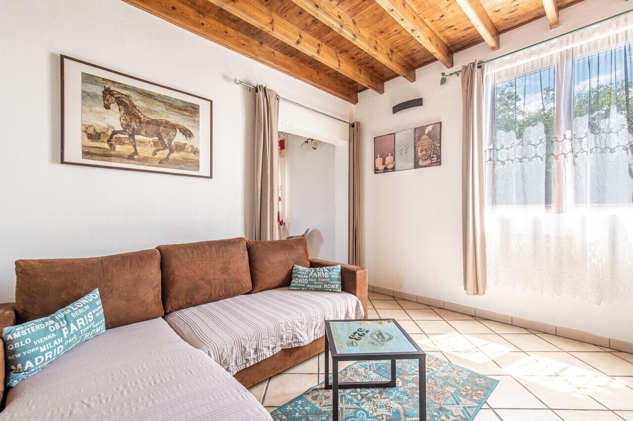 Ein Zimmer mit Holzboden, einem braunen Sofa, einem kleinen Tisch und einem Fenster mit Vorhängen.