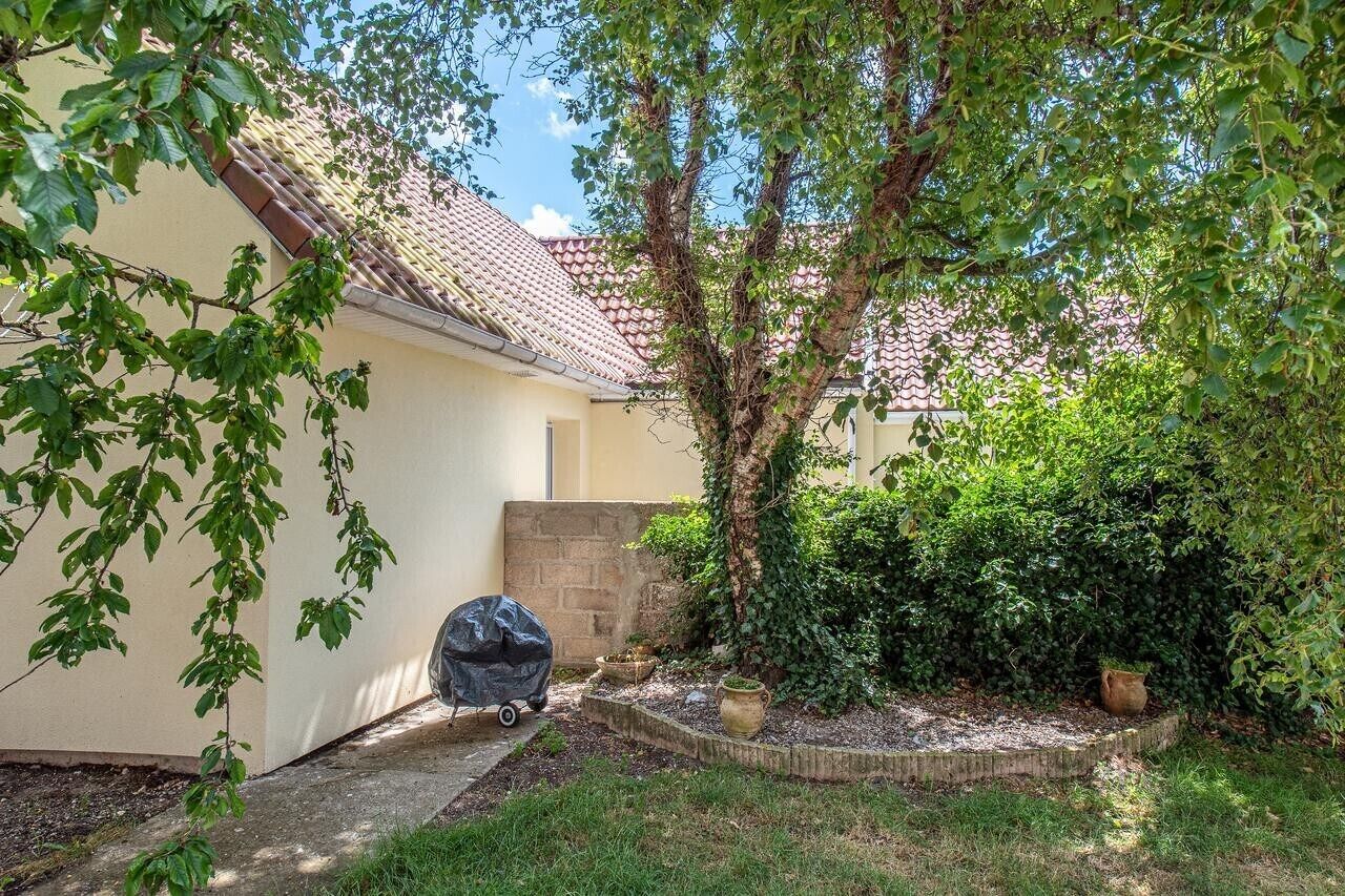 Un jardin arrière d’une maison, avec un arbre, un barbecue et un petit espace aménagé en jardin.
