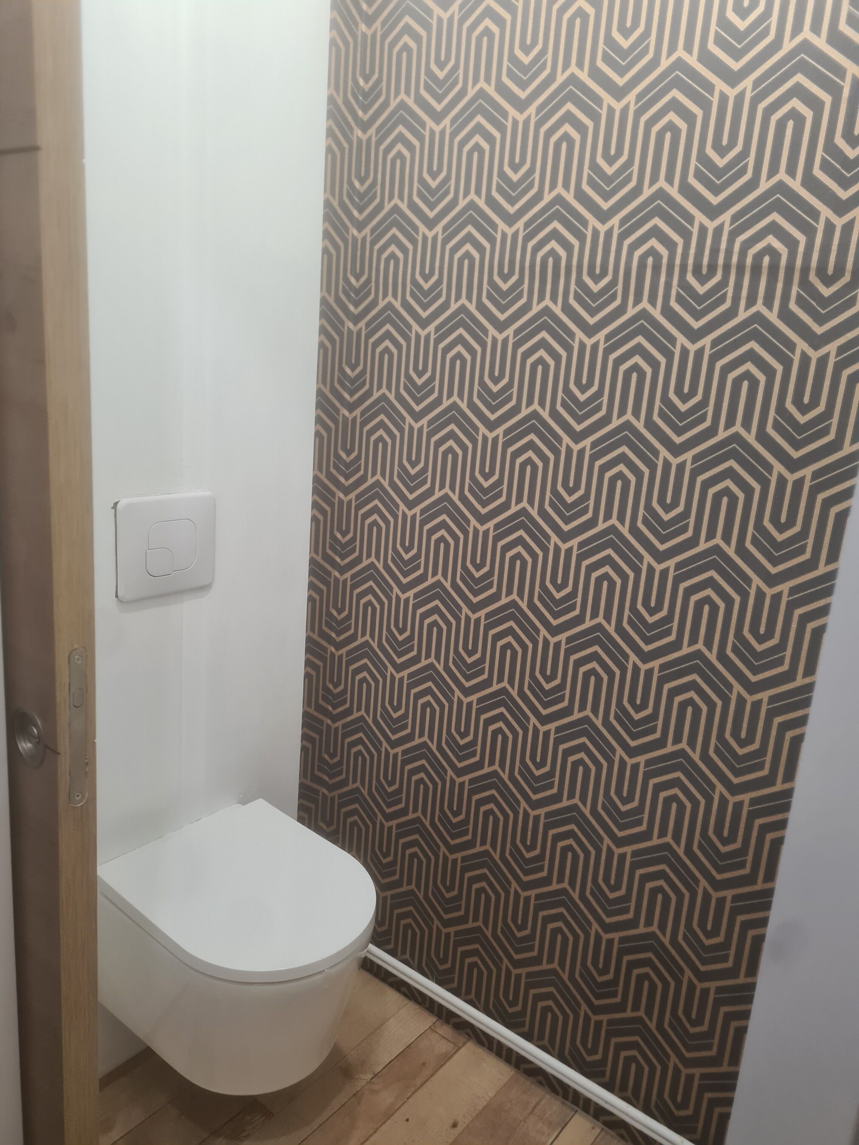 Une petite salle de bain avec des toilettes blanches, un mur à motifs et un plancher en bois.