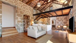 A spacious living area with a stone wall, wooden staircase, a sofa, and a TV.