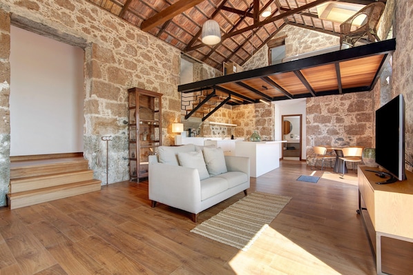 A spacious living area with a stone wall, wooden staircase, a sofa, and a TV.