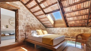 A bedroom with a sloped ceiling, a bed, a chair, and a view of the outdoors.