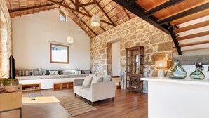 A spacious living area with a stone wall, wooden beams, a sofa set, a coffee table, and a fireplace.