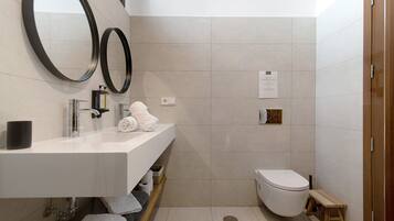Un baño moderno con un lavamanos blanco, dos espejos, un inodoro y un taburete de madera.