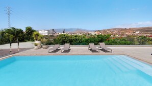 A swimming pool with lounge chairs, a clear sky, and a distant view of buildings and hills. - Country House 'Iris - Finca La Suerte Grande' with Mountain Views and Wi-Fi (Telde)