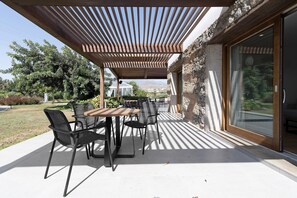 An outdoor patio with a table and chairs, a pergola overhead, and a view of the landscape.
