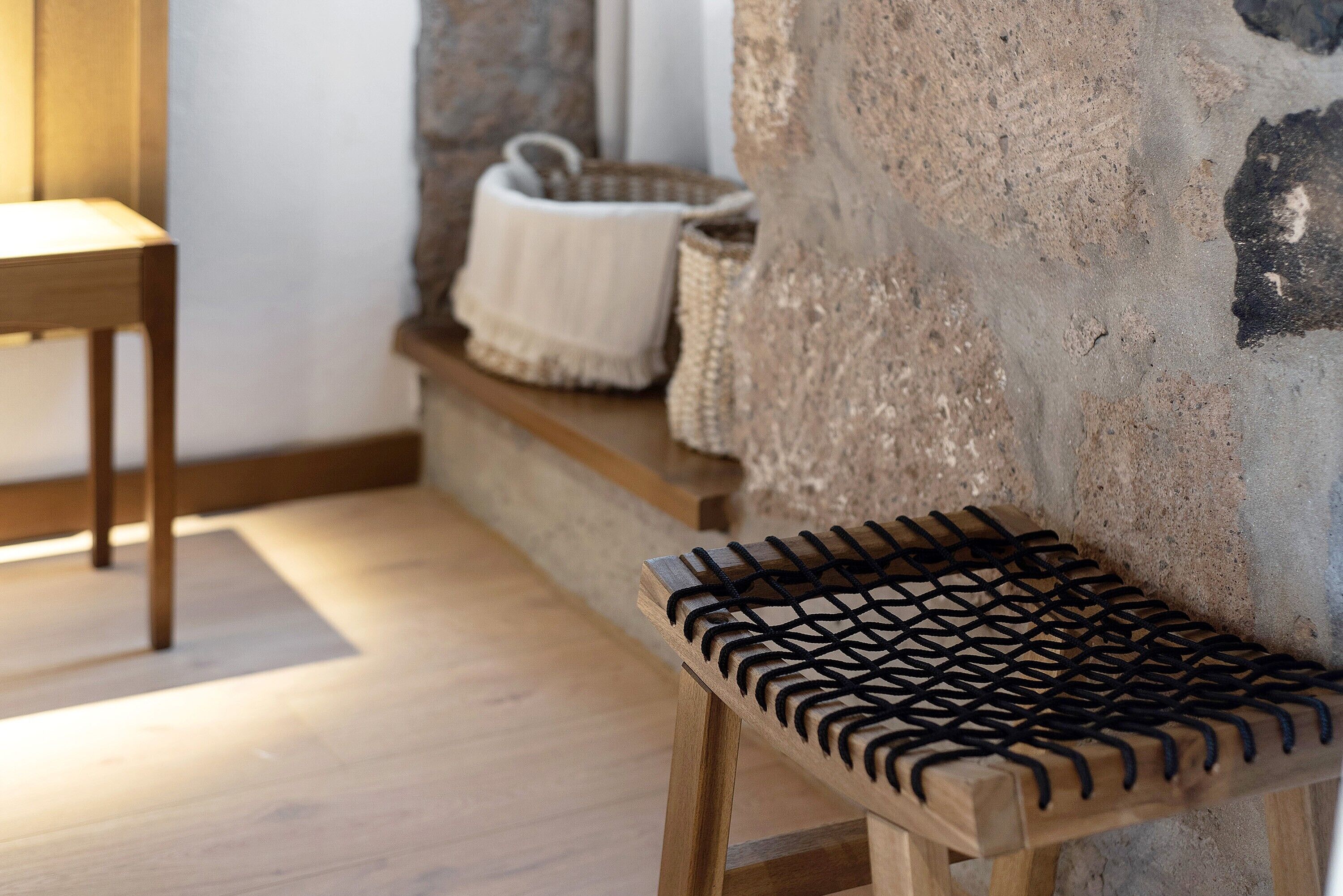 Un banco de madera con asiento de malla negra, una pared de piedra y suelo de madera.