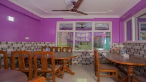 A dining area with purple walls, a large window, and a ceiling fan. - MeroStay 117 Siddhi Binayak Hotel (Tohka)