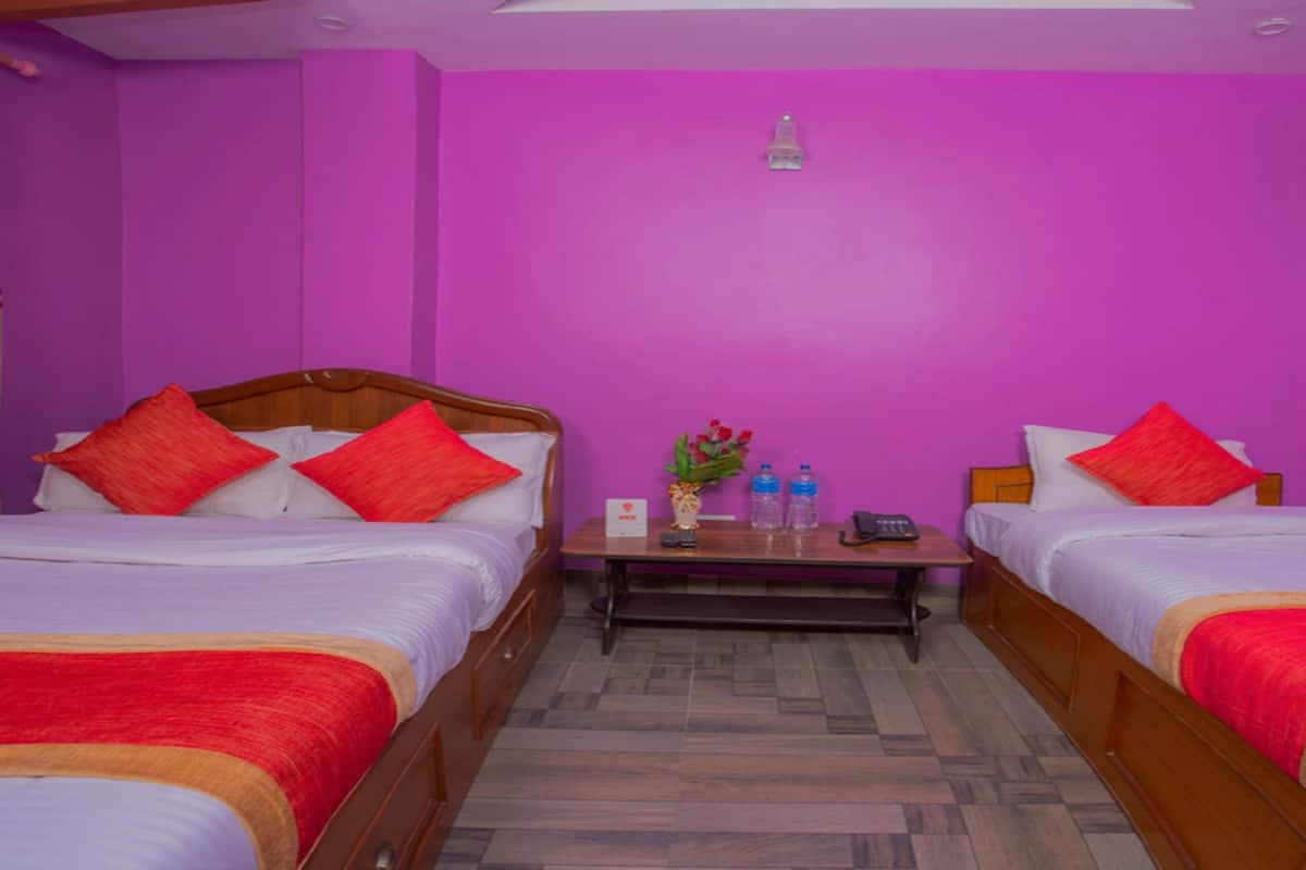 A room with two beds, each with red and white bedding, a small table with a vase and bottles, and a ceiling light.