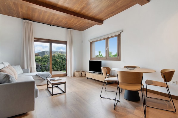 A modern living room with a sofa, coffee table, TV, and dining area with chairs and a table.