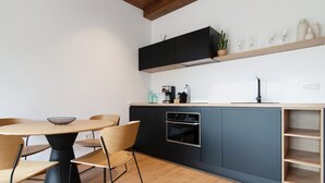 A modern kitchen with a round dining table, chairs, a built-in oven, and a wooden shelf above the counter. - Holiday Home 'Musa - Finca La Suerte Grande' with Mountain Views and Private Terrace (Telde)