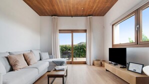 A modern living room with a sofa, coffee table, TV, and a view of greenery through a sliding door. - Holiday Home 'Musa - Finca La Suerte Grande' with Mountain Views and Private Terrace (Telde)