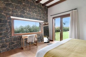 Een slaapkamer met een stenen muur, een groot raam, een bed, een bureau en een stoel.