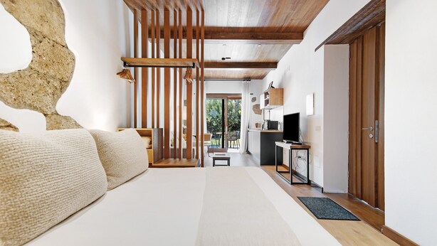 Ein Schlafzimmer mit einem großen Bett, Holzbalken, einer Steinwand, einem Schreibtisch und einem Fernseher.