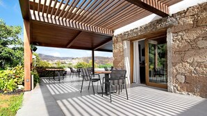 Eine Terrasse im Freien mit einer Holz-Pergola, Steinmauern und Blick auf die Landschaft.