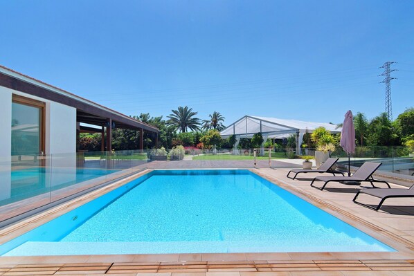 A rectangular swimming pool with clear blue water, surrounded by a wooden deck and lounge chairs.