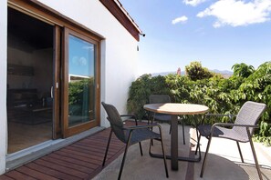Een buitenpatio met een tafel en stoelen, een schuifpui naar een kamer en uitzicht op groen en verre bergen.