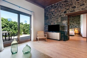 A modern living room with a stone wall, a flat-screen TV, a wicker chair, and a wooden floor.