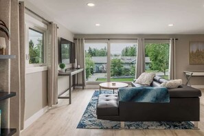 A modern living room with a dark sofa, a round coffee table, and a blue rug. - Beautiful 3BDR Home steps away from Parks & Trails (Anchorage)