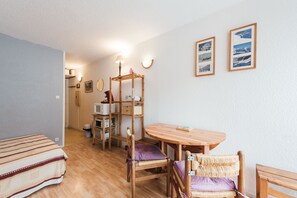 Una habitación compacta con cama, una mesa de madera, una silla, un pequeño estante con objetos y cuadros en la pared.