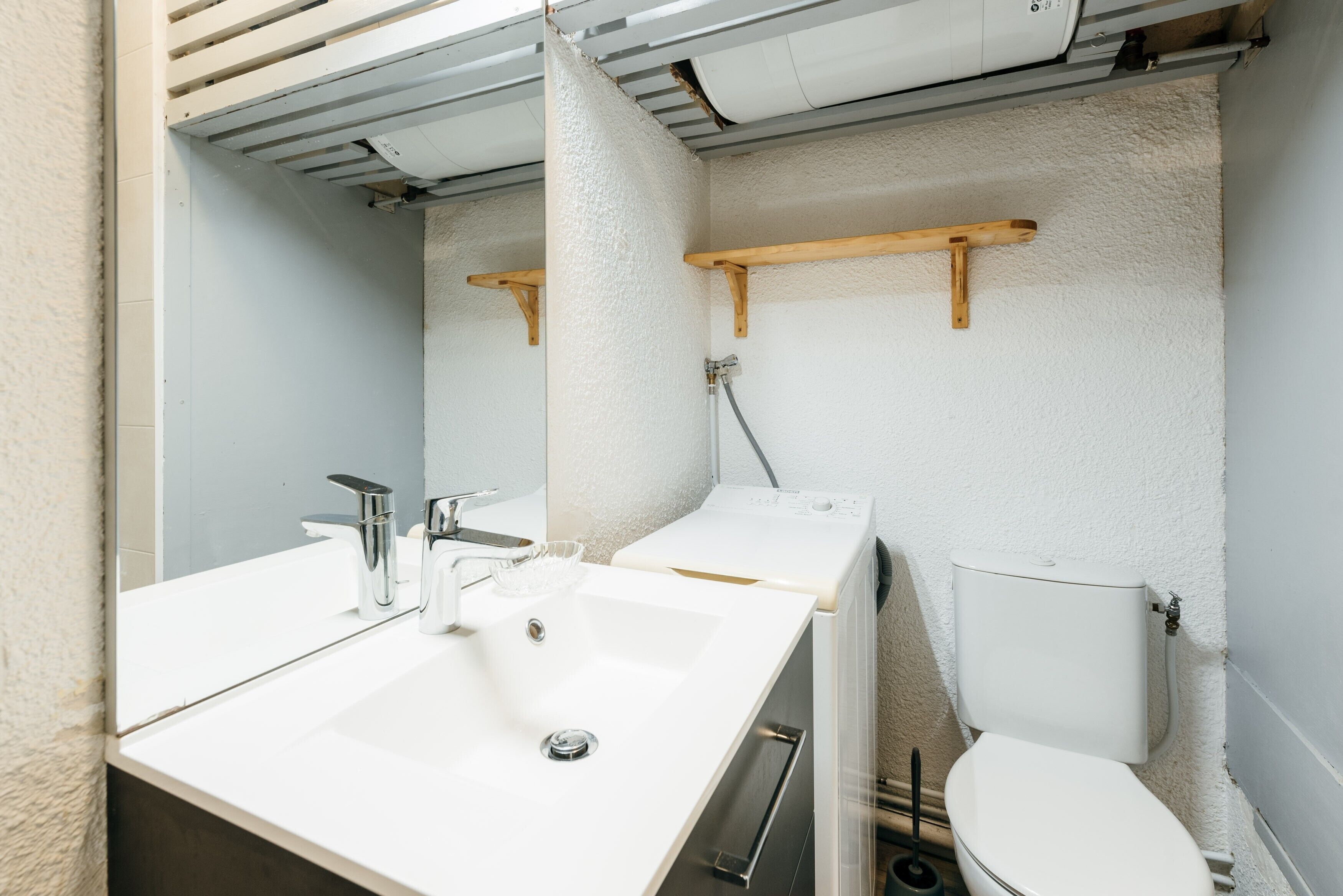 A bathroom with a white sink, a mirror, a toilet, and wooden shelves.