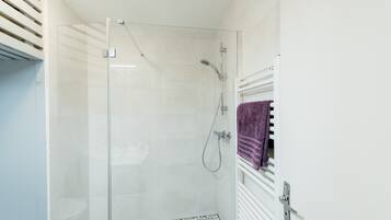 A glass-enclosed shower with a white tiled floor, a white radiator, and a purple towel hanging on the radiator.