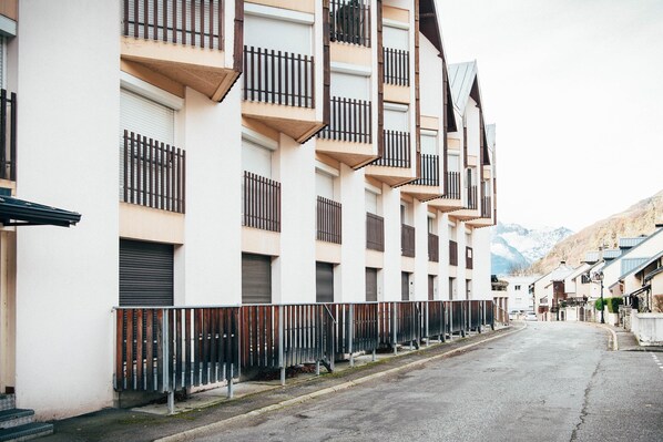 A row of modern buildings with balconies, a street, and mountains in the background.