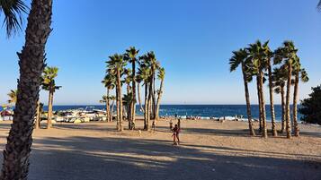 Una playa con palmeras, barcos y gente.
