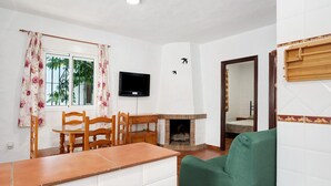 Ett rum med ett matbord, stolar, en platt-TV, en öppen spis och en grön soffa.