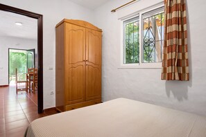 A bedroom with a bed, a wooden wardrobe, a window with curtains, and a view of greenery outside.