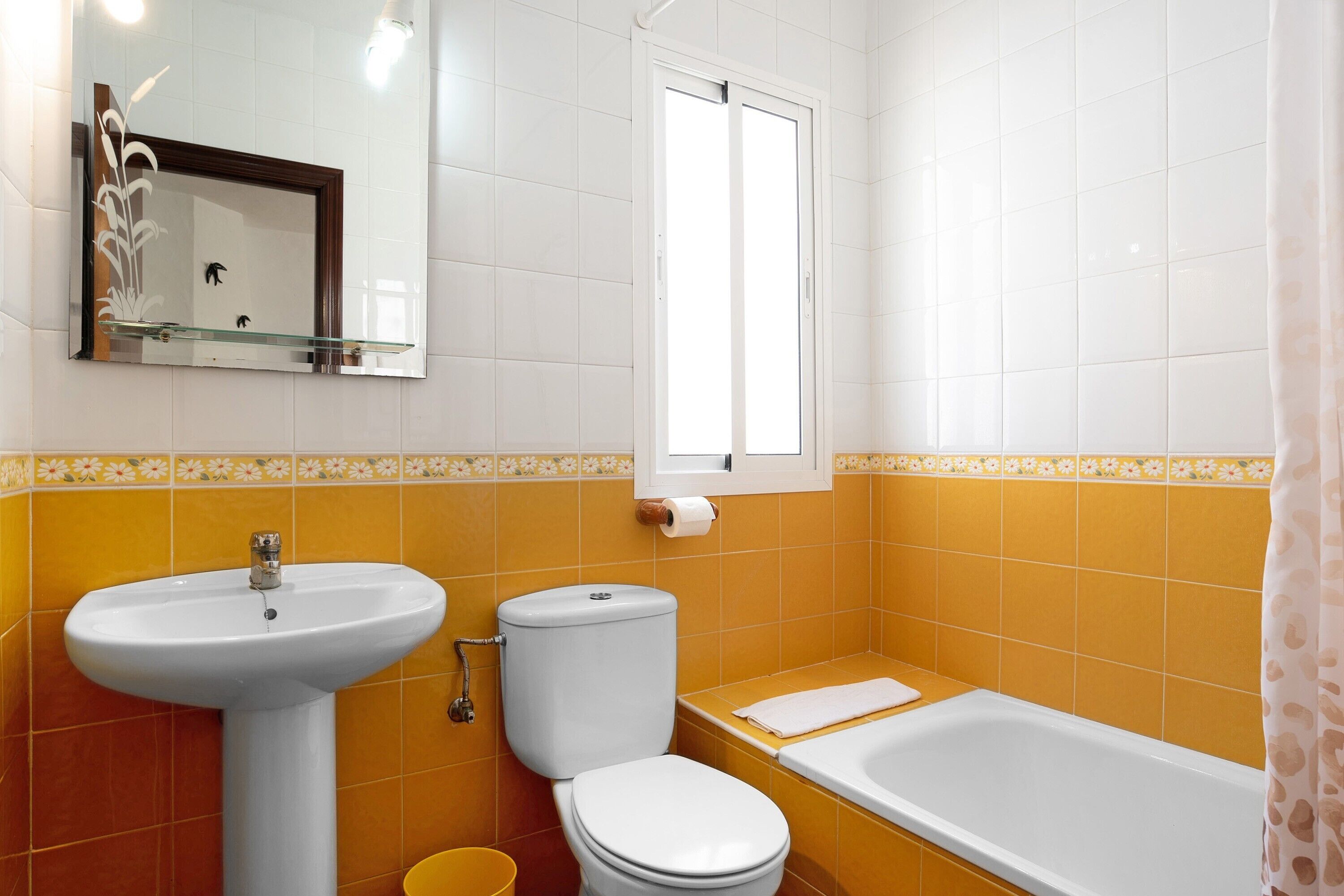 Ein Badezimmer mit Waschbecken, Toilette und Badewanne, mit gelben und weißen Fliesen.