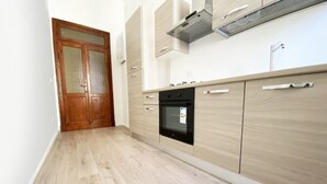Een smalle keuken met houten vloeren, een inbouwoven en lichtgekleurde kastjes.