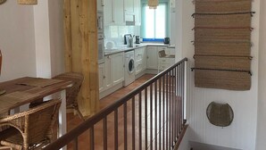 Une cuisine moderne avec des meubles blancs, un séparateur en bois et un coin repas doté de meubles en osier.