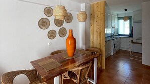 Un coin repas avec une table en bois, des chaises en osier, un grand vase orange et des décorations murales tissées.
