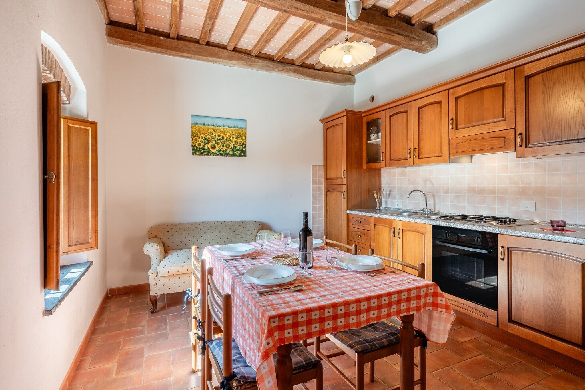 A kitchen with wooden cabinets, a dining table set for four, and a painting of sunflowers on the wall.