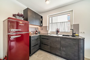 Una cucina moderna con un frigorifero rosso, mobili scuri, una finestra con tende e un lavello.