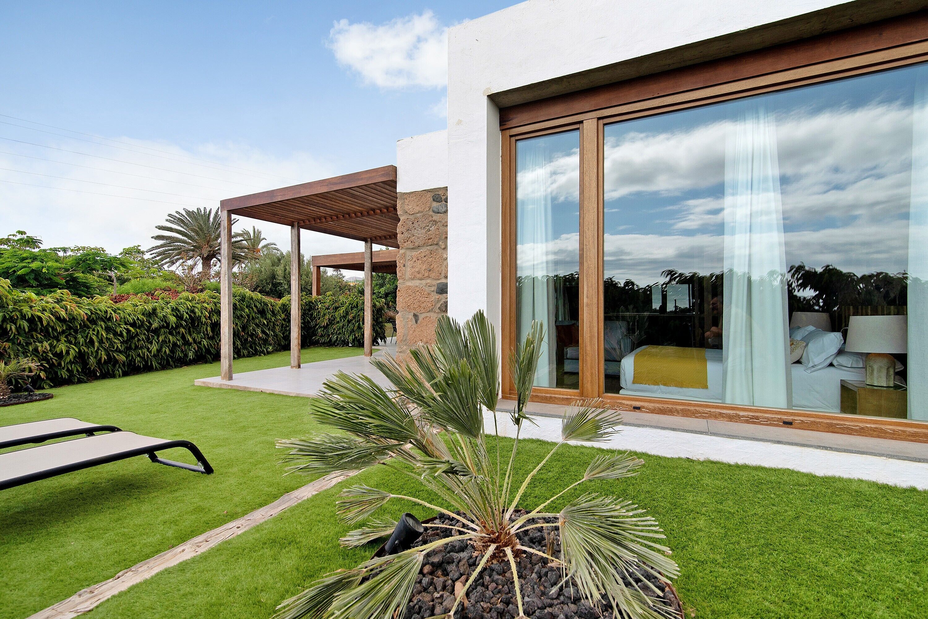 A modern house with a large glass window, a patio with a wooden pergola, and a well-maintained lawn.