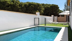 Piscina rectangular con agua cristalina, rodeada por un muro blanco y una valla.