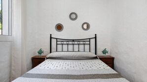 Una cama con colcha estampada, cabecera con espejos circulares y dos mesitas de noche con figuras decorativas de peces.