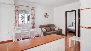 Una sala de estar con sofá, una mesa de comedor con sillas, una zona de cocina con mostrador, y un dormitorio con cama.