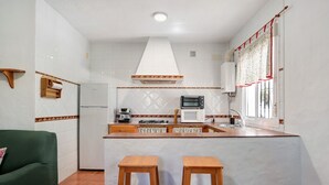 Een keuken met een witte betegelde spatwand, een magnetron, een fornuis en een spoelbak. Er staan twee houten krukken voor de toonbank.