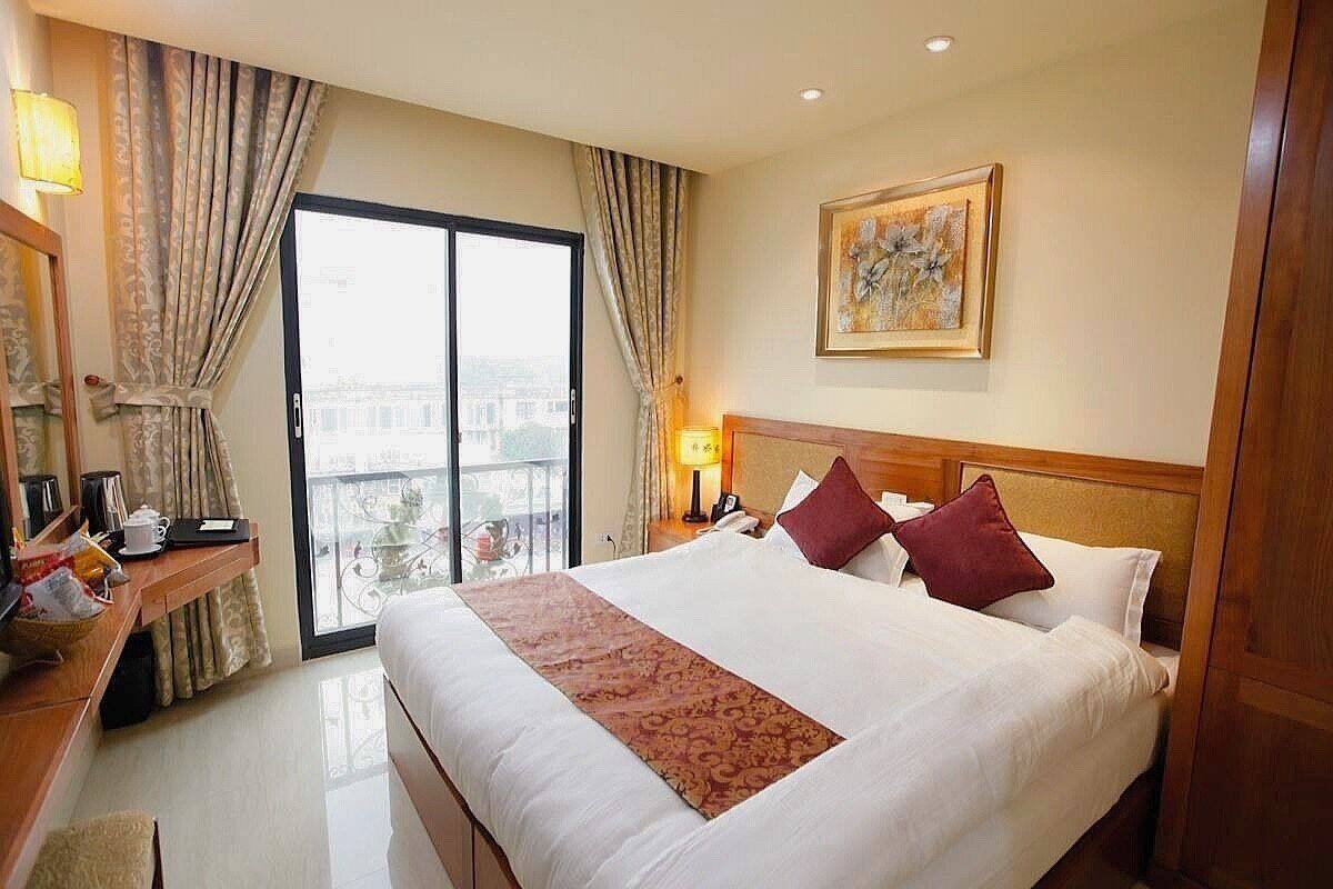 Habitación de hotel con una cama grande, un escritorio con lámpara, un cuadro en la pared y vistas a través de una puerta corredera.