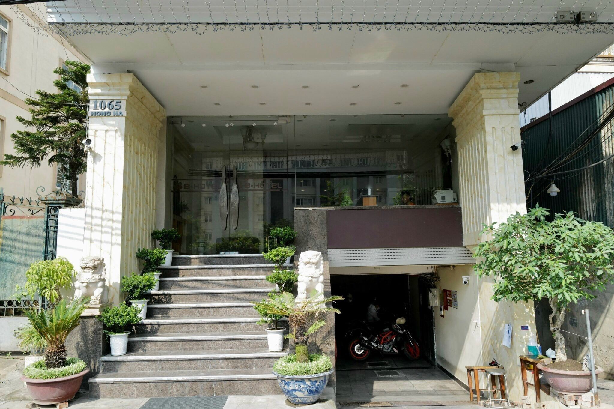 L’entrée d’un hôtel, avec un escalier menant au hall, est agrémentée de plantes en pot et d’une statue.